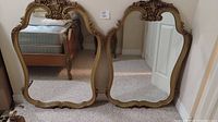 Two wooden framed hanging mirrors leaning against the wall showing overall size and shape.