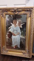 Full view of larger framed picture showing lady in white dress with angel figure and ornate gold frame
