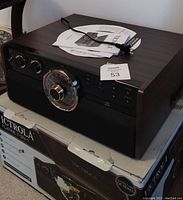 View of full Victrola turntable unit on top of original packaging with instruction manuals and remote control on top