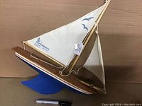 Side view of wooden pond boat showing blue painted hull, wooden deck, and rigged white sails with blue graphics.