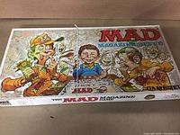 Top of the MAD Magazine board game box showing colorful caricature artwork of Alfred E. Neuman and other characters playing the game with play money.