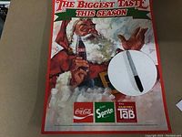 Full view of Coca-Cola Santa cardboard display with text and logos visible; fold out stand partly visible at the back
