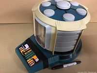 Front and side view of the plastic Star Trek TNG Transporter toy showing the control panel decal, transparent window, and blue-beige color scheme.
