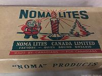 Box close-up showing colorful graphics with Santa Claus, NOMA Lites branding, and Canadian production details.