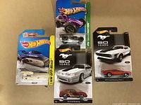 Four Hot Wheels diecast cars on original sealed cards, showing varied models and series.