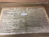 Photo showing front page of The Evening Journal newspaper from 1887, folded in half, with various news and advertisements visible.
