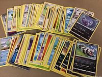Photo showing a lot of 94 Pokemon cards laid out spread on a surface. Many cards are visible, featuring various Pokemon characters with mostly yellow borders.