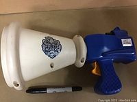 Side view of blue and white plastic embossed toy bullhorn with Police Academy logo and Sharpie for size reference