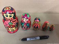 Five wooden Russian nesting dolls sized from largest to smallest with colorful traditional designs placed behind a Sharpie for size comparison.