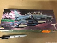 Photo showing the sealed box featuring the detailed illustration of the McDonnell Douglas DA-4M Skyhawk aircraft scale model, with a visible Sharpie marker for size comparison.