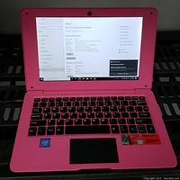 Pink laptop open to About settings screen showing device specifications.