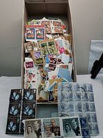 Open shoe box filled with loose and attached British stamps from various territories, visible colorful blocks and individual stamps with postal cancellations.