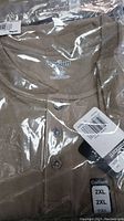 Close-up of Carhartt shirt neckline with brand label, size XL inside but tag on packaging shows 2XL size. 3-button placket visible through sealed plastic packaging.