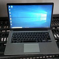 Open laptop on black metal shelf showing display with Windows desktop and keyboard