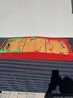 Photo of the tabletop hockey game showing wooden board with red frame and playing field with multiple player figures and goals.