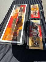 Three abstract paintings laid on a surface in sunlight showing colors and condition.