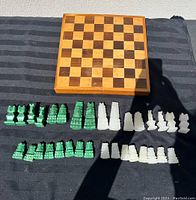 Full view of the wooden chess board with green and white chess pieces laid out in front of it on a black cloth.