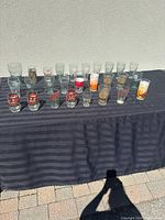 Wide view of 27 assorted Coca Cola glasses on a black cloth including various retro and vintage designs