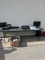 Full view of table with all electronics including laptops, iPad, iPhone, external devices, camcorder, and accessories on a folding table outside.