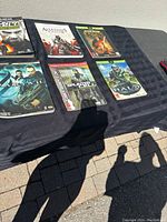 Seven Xbox game guides laid out on a black cloth showing front covers of titles including Halo 3, Assassin's Creed II, and Splinter Cell.