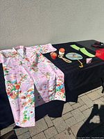 Full layout of pink kids kimono size 40 with floral pattern and all accessories including shoes, fans, temari balls, and obi belt on black cloth
