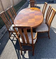 View of the full oval wood dining table surrounded by eight chairs, showing the wood grain pattern and chair styles.