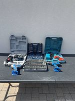 Overview of lot with power tools and metal tap and die sets arranged on table outdoors