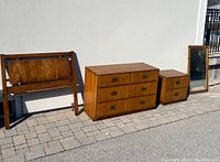 Full set of Dixie Campaigner bedroom furniture including single bed headboard, dresser, nightstand, and mirror displayed outside on pavement.