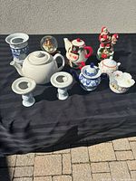 Full view of the teapots, candle holders, bowl, and decorative holiday items on a black cloth against a light gray wall.
