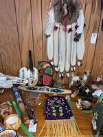 Full view of the lot on a wooden surface showing moccasins, dreamcatcher, Thunderbird carving, beaded belt, rain stick, and other small carvings.