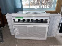 Front view of white Toshiba window air conditioner with extendable side panels for window mounting