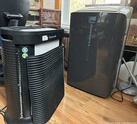 Side and front view of Honeywell air purifier and Dandy Premiere air conditioner units placed on wooden floor.