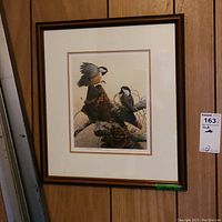 Full view of the framed print featuring two birds with naturalistic details and colors, hung on a wood-paneled wall.