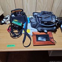 Wide shot of lot items on wooden table, showing Sanyo camcorder, Canon camera in case, battery charger, digital photo frame with remote and adapter.