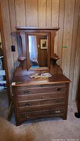 Front view of wood dresser with attached mirror, three drawers, and additional handles on top.