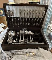 Open wooden flatware chest showing the set of assorted forks, knives, spoons, serving utensils including one Birks sterling silver spoon.