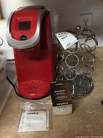Front view of the red Keurig coffee maker, metal coffee pod stand, and Keurig water filter package on kitchen counter.
