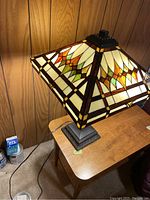 Stained glass lamp on wooden table showing shade illuminated against wood panel wall.