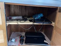 GE clock radio, power adapters and closed laptop on wooden shelf