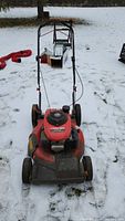 Front view of a red Honda Troy-Bilt gas lawn mower with visible engine cover and starting mechanism on snow-covered ground