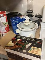 Magic Bullet blender, digital kitchen scale, slow cooker, toaster, multi grater, apple peeler all visible on countertop.