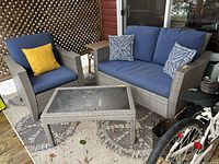 Overall view of gray wicker armchair, loveseat with cushions and glass-top table