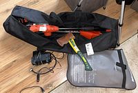 Black & Decker pole saw, charger, black carrying bag, Yardworks hatchet with green/yellow handle, car plug tire pump, and Motomaster booster cables case visible.