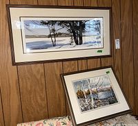 Two framed, matted paintings hanging and leaning against a wood-paneled wall, showing their overall sizes and framing style