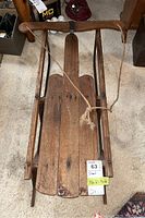 Top-down view of vintage wooden sled showing wooden planks, metal runners, and attached rope.