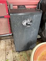 Full view of weathered Bass Pro Shops Masterbuilt electric smokehouse with spotted wear and outdoor setting.