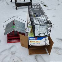 Metal Havahart live animal cage trap on top of its original box, placed on snow with visible surroundings.