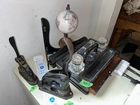 Overview of lot on white surface including two vintage metal punches, globe, wood ink tray with glass inkwell, metal plate holder, and small glass item. Shows wear and use marks.