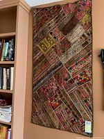 Full view of rectangular quilt hanging on wall beside bookshelf