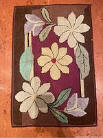 Full view of the antique hooked floral rug with flowers and leaves on burgundy and brown background.